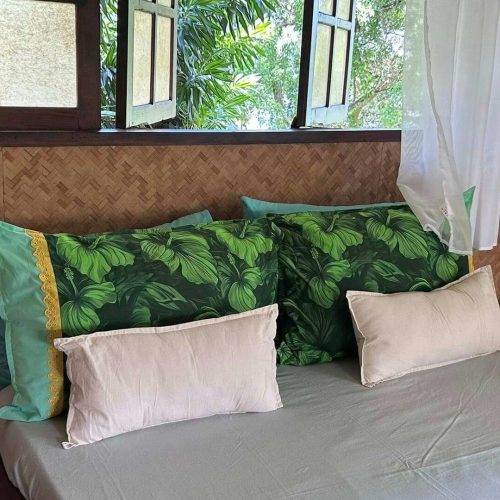 L'arrière du lit du bungalow Hanamio Hill avec la fenêtres semi ouvertes et des taies d’oreiller fleuries