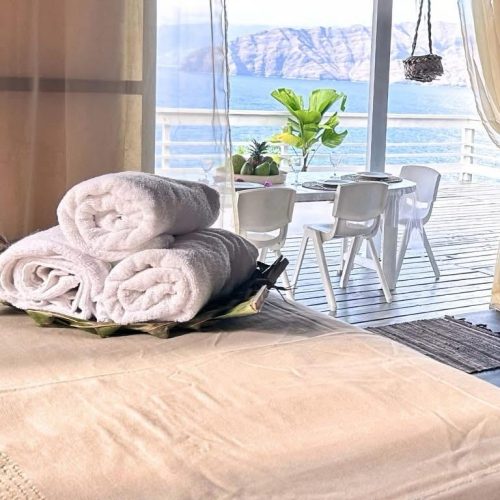 Vue sur la mer depuis le lit du bungalow Hanamio Bay avec serviettes enroulées.